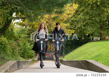 Trendy fashinable teenagers riding public rental electric scooters in urban city park. New eco-friendly modern public city transport in Ljubljana, Slovenia 72225230