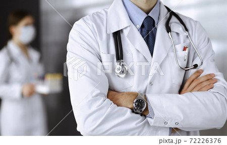 Unknown male doctor in protective mask standing with arms crossed in clinic. Medicine concept during Coronavirus pandemic. Covid 2019 Unknown male doctor in protective mask standing with arms crossed in clinic. Medicine concept during Coronavirus pandemic. Covid 2019 72226376