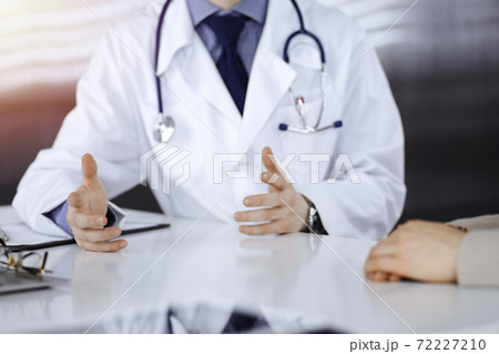 Unknown male doctor and patient woman discussing something while sittingin a darkened clinic, glare of light on the background. Close-up of hands 72227210