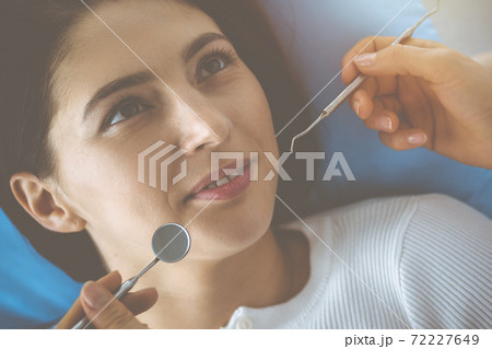 Smiling brunette woman being examined by dentist at dental clinic. Hands of a doctor holding dental instruments near patient's mouth. Healthy teeth and medicine concept 72227649