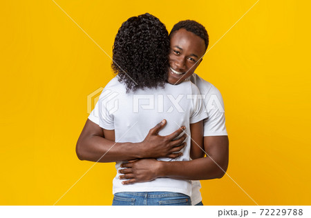 Happy black guy hugging his girlfriend, yellow background Happy black guy hugging his girlfriend, yellow background 72229788