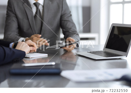 Unknown businessman using tablet computer and working together with his colleague while sits at the glass desk in modern office. Teamwork and partnership concept 72232550