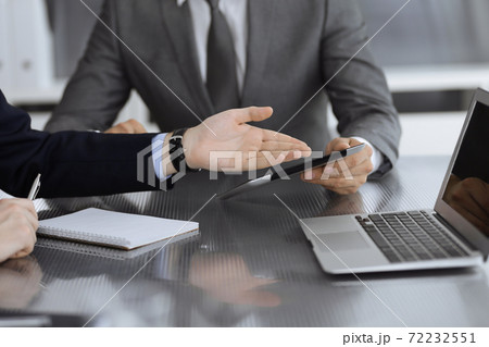Unknown businessman using tablet computer and working together with his colleague while sits at the glass desk in modern office. Teamwork and partnership concept 72232551