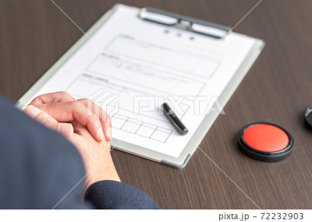 書類にハンコを押すことを躊躇するミドルのビジネスマンの手元 72232903