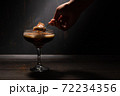 A woman's hand with a spoon takes jelly coffee with milk in a glass bowl, which is sprinkled with chocolate chips. Deep shadows. Rustic. 72234356