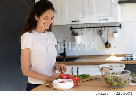 Smiling attractive woman cutting fresh vegetables in modern kitchen Smiling attractive woman cutting fresh vegetables in modern kitchen 72235001