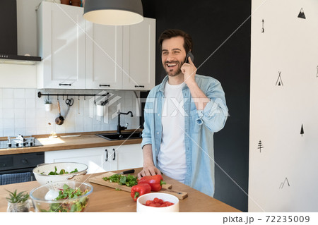 Overjoyed man talking on phone, standing in modern kitchen 72235009
