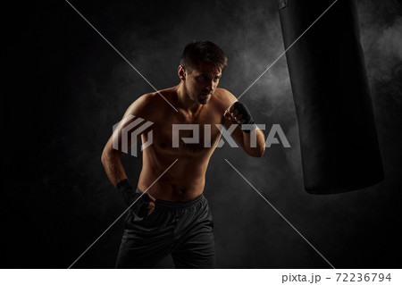Male boxer punching in boxing bag on black background Male boxer punching in boxing bag on black background 72236794