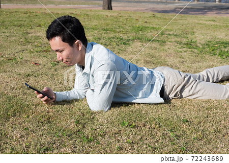 芝生に寝転がりながらスマホを見る男性 72243689