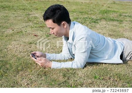 芝生に寝転がりながらスマホを見る男性 72243697