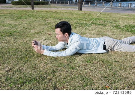 芝生に寝転がりながらスマホを見る男性 芝生に寝転がりながらスマホを見る男性 72243699