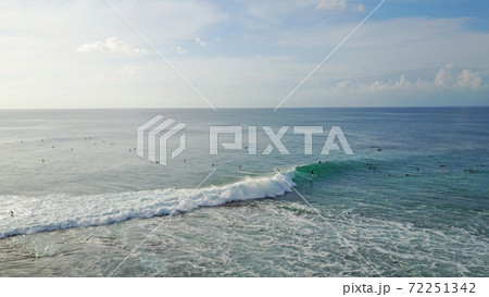 Surfers catch waves at Uluwatu beach, Bali. Huge waves stretch along the beach.  72251342