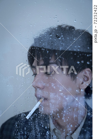 雨の窓際でタバコを吸う男性のポートレートの写真素材