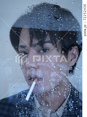 雨の窓際でタバコを吸う男性のポートレートの写真素材