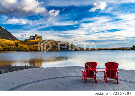 Red chair look over Waterton Lake Marina Point in autumn foliage season sunny morning. Blue sky with colourful clouds reflect on the lake water surface. Waterton Lakes National Park, Alberta, Canada. 72257297