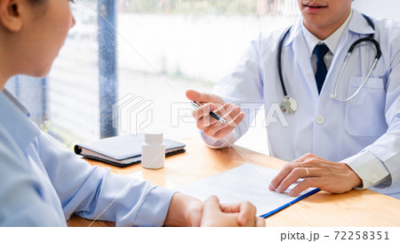 Charming Asian male doctor giving advice and medical informations and diagnosis to a female patient at consulting room in clinic. 72258351