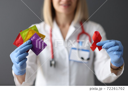 Doctor in protective gloves holding red ribbon and condoms closeup 72261702