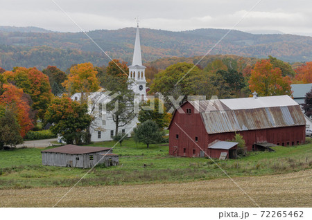 A small church sits on a farm next to a weathered red barn during Autumn 72265462