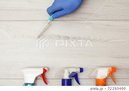 Hand in rubber glove holding dust brush with bottles of detergent Hand in rubber glove holding dust brush with bottles of detergent 72293400