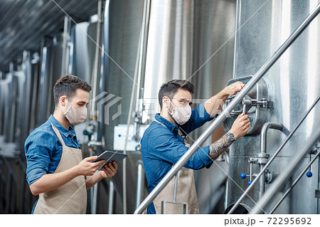 Young attractive workers in aprons and protective masks close vent on kettle Young attractive workers in aprons and protective masks close vent on kettle 72295692