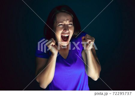 Close up portrait of young crazy scared and shocked woman isolated on dark background Close up portrait of young crazy scared and shocked woman isolated on dark background 72295737