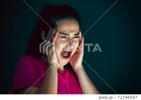 Close up portrait of young crazy scared and shocked woman isolated on dark background Close up portrait of young crazy scared and shocked woman isolated on dark background 72296087