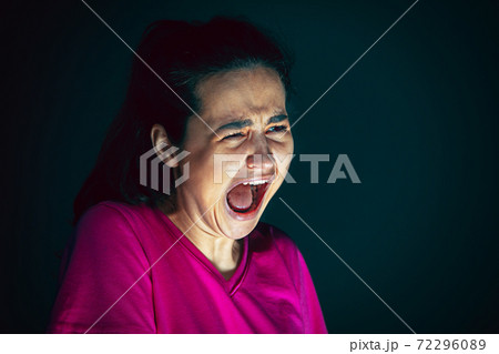 Close up portrait of young crazy scared and shocked woman isolated on dark background Close up portrait of young crazy scared and shocked woman isolated on dark background 72296089