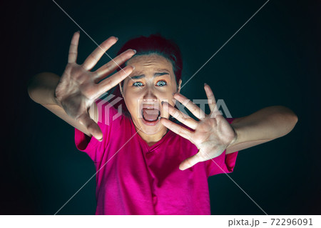 Close up portrait of young crazy scared and shocked woman isolated on dark background 72296091