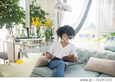 Smiling young woman reading magazine in cozy room 72297231