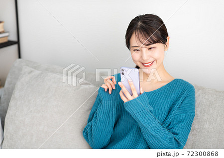 リビングでソファに座ってスマホを使う若い女性 72300868