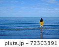 Back side of a girl in yellow shirt standing in the sea looking at the horizon. 72303391