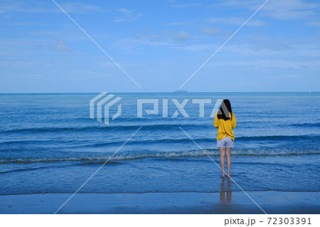 Back side of a girl in yellow shirt standing in the sea looking at the horizon. 72303391