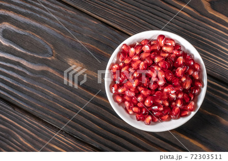 Garnet seeds in white plate on dark wooden background 72303511