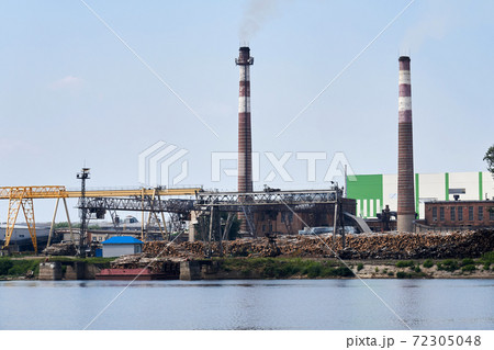industrial landscape, pulp and paper mill with stacks of logs on the river bank industrial landscape, pulp and paper mill with stacks of logs on the river bank 72305048