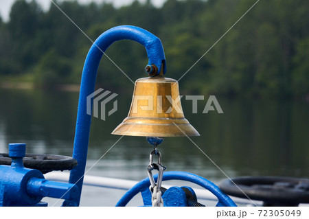 brass bell on the foredeck of a ship against the background of a blurred wooded coast brass bell on the foredeck of a ship against the background of a blurred wooded coast 72305049