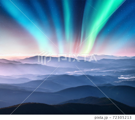 Aurora borealis above the mountain valley in low clouds at night Aurora borealis above the mountain valley in low clouds at night 72305213