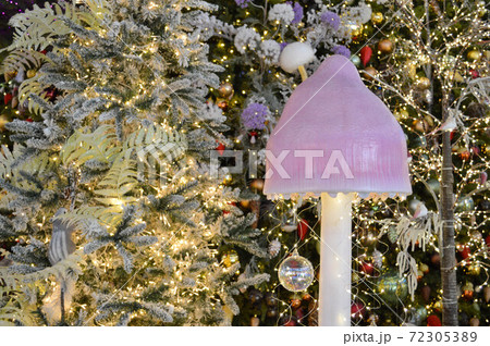 shop window decoration, shopping center decor. artificial white spruce with garlands. beneath them is a mushroom with a large pink cap. cute christmas forest for shop window decor shop window decoration, shopping center decor. artificial white spruce with garlands. beneath them is a mushroom with a large pink cap. cute christmas forest for shop window decor 72305389