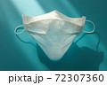 Medical mask folded in the shape of a face in the sunlight on a turquoise background 72307360