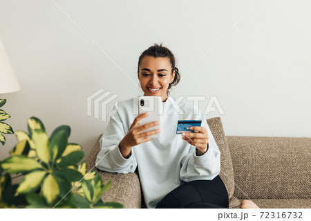 Smiling woman using smartphone and credit card. Young female making a purchase online. Smiling woman using smartphone and credit card. Young female making a purchase online. 72316732