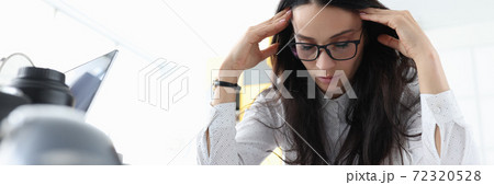 Woman sits with her eyes closed and holds her head in office. 72320528