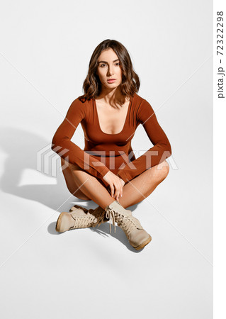 Pretty young woman in brown bodysuit and suede boots sits on the floor 72322298