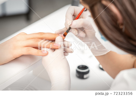Manicurist covering nails with transparent polish 72323356
