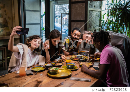 Five young friends sitting at the table in a cafe, taking selfie 72323623