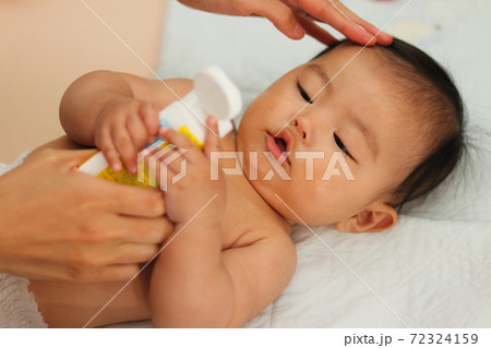 お風呂上りの赤ちゃんに保湿クリームを塗るの写真素材