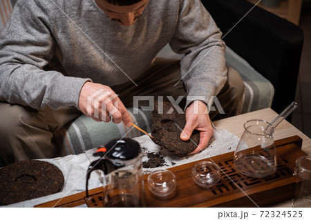 A man prepares raw ripe tea for a tea ceremony. Picks out a piece of tea with a tea needle. Hands close-up. A man prepares raw ripe tea for a tea ceremony. Picks out a piece of tea with a tea needle. Hands close-up. 72324525