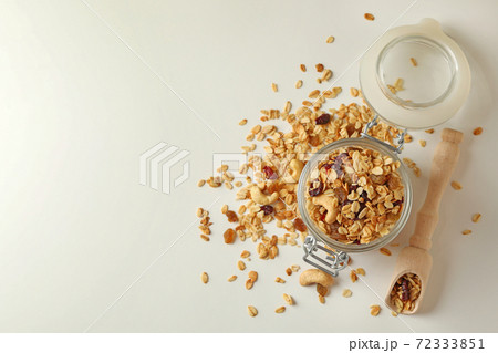 Glass jar and scoop with granola on white background Glass jar and scoop with granola on white background 72333851