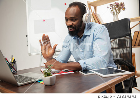 Online english courses at home. Smiling man teaches students remotely in interior of living room Online english courses at home. Smiling man teaches students remotely in interior of living room 72334243