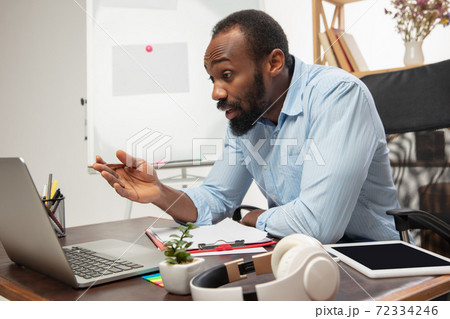 Online english courses at home. Smiling man teaches students remotely in interior of living room Online english courses at home. Smiling man teaches students remotely in interior of living room 72334246