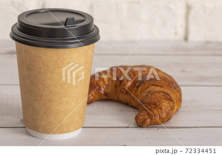 Paper cup of coffee and croissant on a wooden table. Light background. 72334451