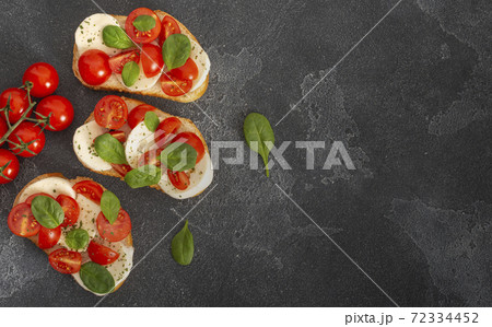 Caprese bruschetta toasts with mozzarella, cherry tomatoes and fresh garden basil.Traditional italian appetizer or snack, antipasto. Top view with copy space. Flat lay. 72334452